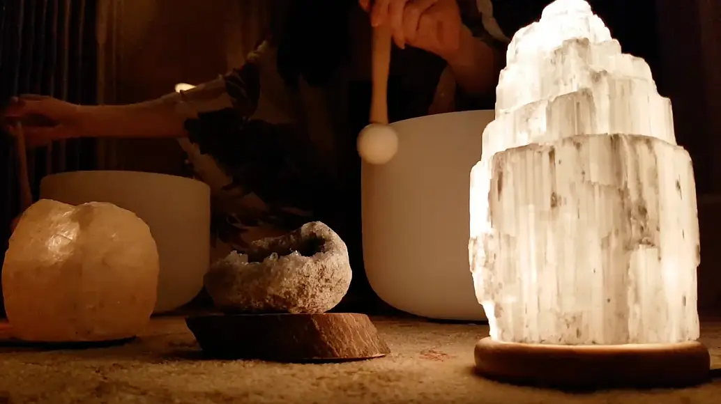 Woman playing crystal sound-healing bowls next to a salt lamp.